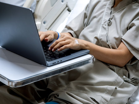 Patient in hospital using laptop for remote work while recovering, showing concept of healthcare flexibility, teleworking, and digital lifestyle integration during medical treatment or recovery.の写真素材
