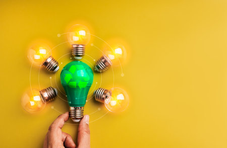 Green light bulb with recycle symbol surrounded by glowing bulbs on yellow background, representing...