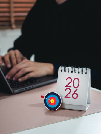 2026 Desk calendar with 3d target dart icon and businessperson working with laptop, representing new year business goals, strategic planning, business and technology trends, data researching online.の写真素材