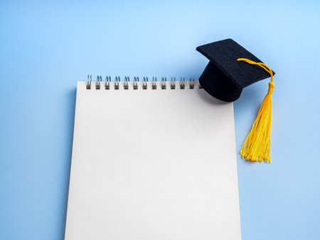 White blank notebook with black graduation cap on blue background. Concept for education planning, study goals, to-do list for students, congratulations note, academic success, learning objectives.の写真素材