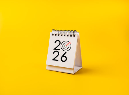White 2026 desk calendar with target dart icon isolated on yellow background. Concept for new year planning, business goals, success, future trends, target setting, strategy, and achievement.の写真素材