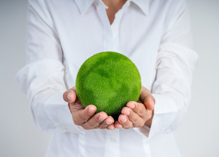 Person in white shirt holding green grass globe in hands representing the Earth, symbolizing environmental care, sustainability, and eco responsibility. Concept for Earth Day, green business, and CSR.の写真素材
