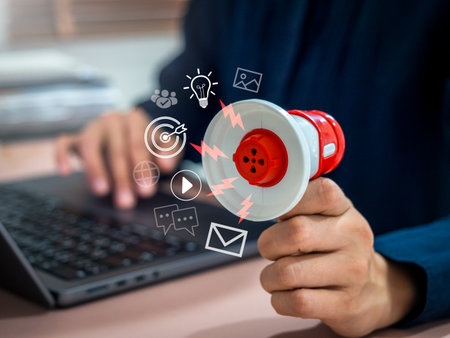 Businessman holding megaphone with digital marketing icons while working on laptop, representing business strategy, online promotion, social media advertising, and content marketing communication.の写真素材