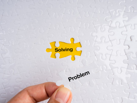 Hand placing a white puzzle piece labeled âProblemâ into a yellow missing spot revealing the word âSolving.â Concept of problem-solving, strategy, logic, solution, and fixing issues.の写真素材