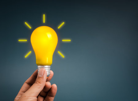 Hand holding glowing yellow light bulb symbolizes creative idea, innovation, inspiration, brainstorming, solution concept, startup thinking, and bright vision for business or personal development.の写真素材