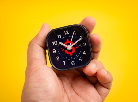 Hand holding a small clock with red dollar symbol on black face. Concept of time is money, business efficiency, time management, financial planning, deadline pressure, and maximizing profit per hour.の写真素材