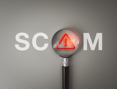 Magnifying glass highlighting on red warning sign in the word SCAM represents scam detection, online fraud report, cybercrime prevention, digital theft awareness, scammer, and cybersecurity concept.の写真素材