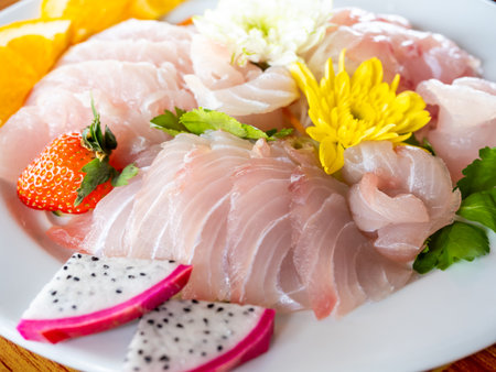 Fresh Thai fish sashimi served with tropical fruits and edible flowers on white plate, representing healthy Japanese cuisine, clean eating, and fusion food culture with local Asian ingredients.の写真素材