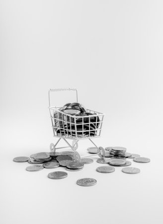Mini shopping cart filled with coins on white background represents profit, sales revenue, cost...