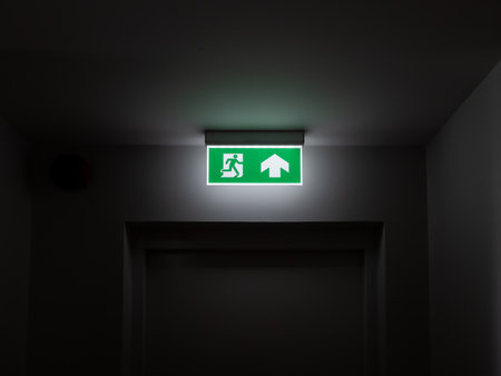 Emergency exit sign glowing in dark hallway, symbolizing building safety, fire escape route,...