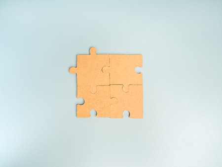 Four blank wooden puzzle pieces fitting together on blue pastel background represent teamwork, collaboration, connection, and business team building. Ideal for leadership and strategy concepts.の写真素材