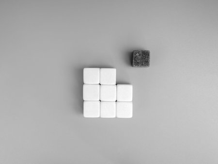 One dark cube placed apart from a group of white cubes on grey background. Uniqueness, leadership, individuality, and standing out from the crowd. Perfect for concept of diversity and innovation.の写真素材
