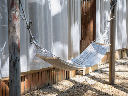 Empty hammock under soft morning sunlight in a peaceful outdoor setting, with warm tones, pebbled floor, and sheer curtainsâperfect scene for rest, calm, and slow living inspiration.の写真素材