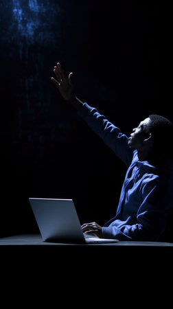 Man with raised hands at table with laptopの素材