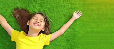 A young girl is lying down on a field covered with lush green grass. She appears and relaxed content, enjoying the connection with nature.の素材