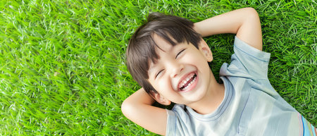 A young boy is lying on top of a vibrant green field, surrounded by the beauty of nature. The grass is rich and healthy, creating a tranquil backdrop for the boys relaxed posture.の素材