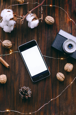 Brown wood background with texture. Decorative nuts and fir cones. Minimalist style. Photo camera. Smartphone with place for quotes. Xmas and Happy New Year composition. Flat lay, top viewの写真素材