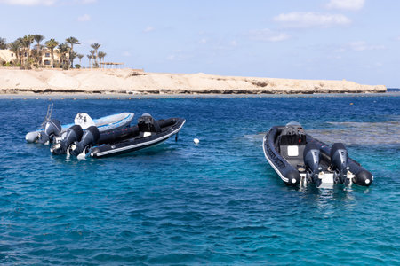 Three inflatable boats sit empty at anchor on a coral reef with crystal clear water.の写真素材