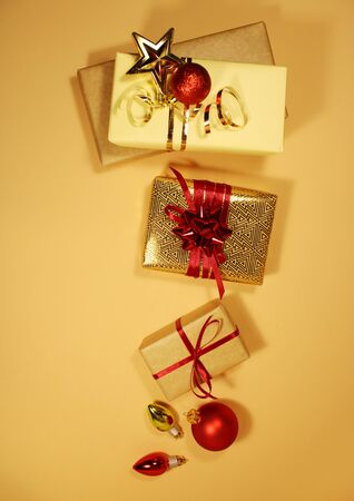 Composition of Christmas gift boxes decorated with golden tinsel, sparkles, red matte balls and bows on a beige background. Place for textの写真素材