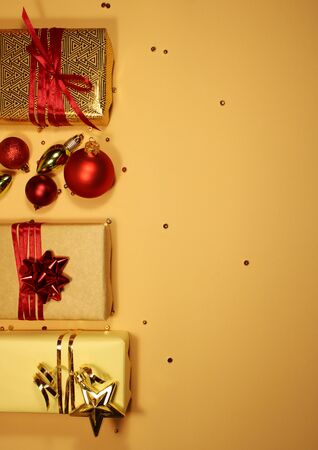Composition of Christmas gift boxes decorated with golden tinsel, sparkles, red matte balls and bows on a beige background. Place for textの写真素材