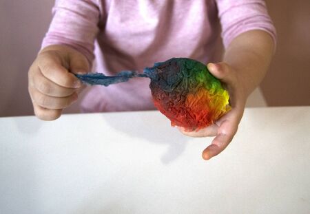 An Easter egg in the girls hands. The process of staining the Easter egg in bright blue, red, yellow, green. Conscious children. Creative process and preparation for the spring holidayの写真素材