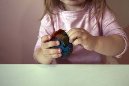 An Easter egg in the girls hands. The process of staining the Easter egg in bright blue, red, yellow, green. Conscious children. Creative process and preparation for the spring holidayの写真素材