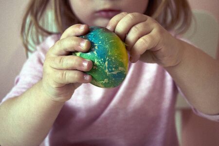 An Easter egg in the girl's hands. The process of staining the Easter egg in bright blue, red,...