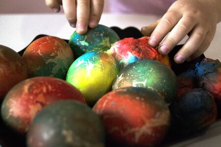 Caring childrens hands put painted Easter eggs in a plate. Easter eggs are bright in color and with an abstract pattern. Preparing for the religious holiday of Easter.の写真素材