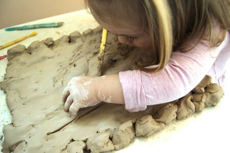 little girl works with clay at the table. Time for childrens creativity. Clay petal with a baby. Previously, the development of the child. A Conscious Childhoodの写真素材