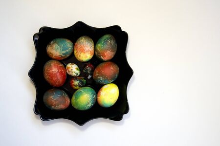 A group of brightly colored Easter eggs on a black curly plate on a white background. A place for text. Easter. Creative abstract painting of eggs.の写真素材