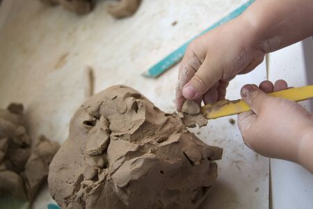 The hands of a small child work with a piece of gray clay on a white table. View from above. Favorite family hobby. Early child development.の写真素材