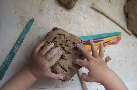 The hands of a small child work with a piece of gray clay on a white table. View from above. Favorite family hobby. Early child development.の写真素材