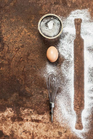 Baking utensils and ingredients. Eggs, flour, whisk and rolling pin on an old vintage background....