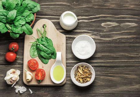 Ingredients for preparing salad on a wooden background. Vegetable salad in a bowl, tomato, spinach, garlic, olive oil. Healthy, clean food concept. Vegan or gluten-free diet. Copy spaceの写真素材