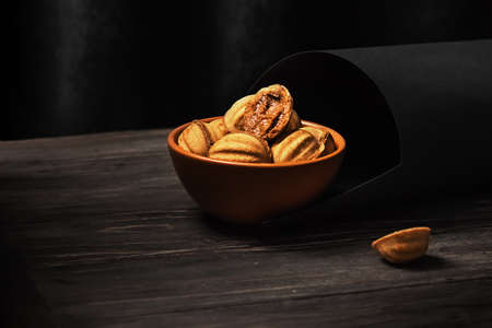 Delicious shortbread cookies in the shape of a walnut seasoned with sweet condensed milk in a clay plate on a wooden background. Homemade cakes, dessert. Dark background, selective focusの写真素材