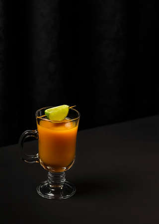 Glass of orange juice with lime on a dark background. Modern composition, copy space.