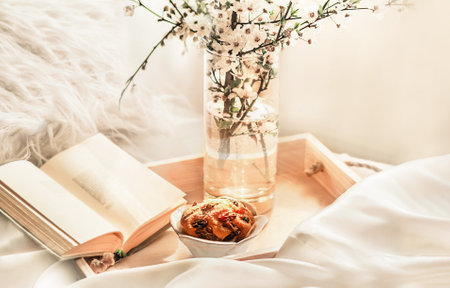 The atmosphere of a romantic morning, coffee in bed. Flowering branches in a vase, an open book and a cup of coffee on a wooden tray on a white silk bed. Home interior. Life styleの写真素材