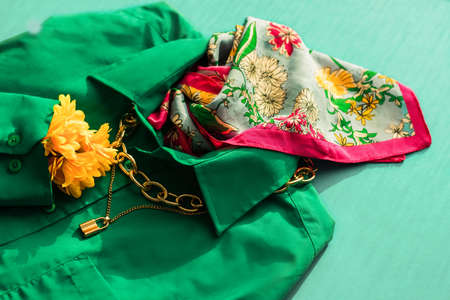 Background with fashionable clothes. Green trendy shirt, chain around the neck and silk scarf on a bright colored background. Beauty and style blog concept.の写真素材