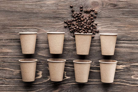 Coffee paper cups and one cup with coffee beans on a wooden background. Pattern and creative background concept for cafes.の写真素材