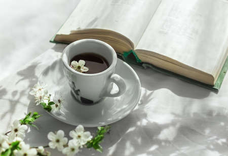 Morning coffee. Blossoming branches, an open book and a cup of coffee on a white table in a garden in Provence style. Home interior. Life styleの写真素材