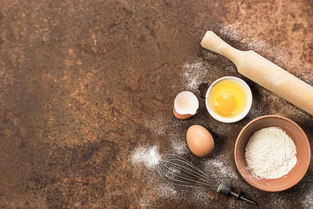 Baking utensils and ingredients. Eggs, flour, whisk and rolling pin on a rusty background. Baking concept, copy space. Food backgroundの写真素材
