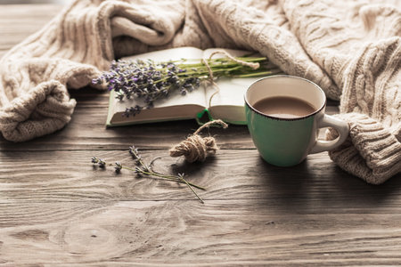 A cup of coffee on a wooden table, an open book and a warm sweater on the background of a bouquet of lavender flowers. Still life concept. Cozy morning.の写真素材