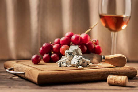 Blue cheese, wine in a glass and a bunch of grapes on a wooden board. Concept for wine and cheese lovers gorgonzola and dor blue, cheese dairy.の写真素材