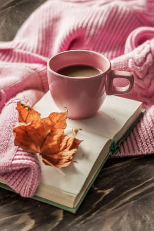 Autumn morning coffee. A cup of coffee on a wooden table and a warm sweater on a background of autumn leaves. Still life concept. Copy space.の写真素材