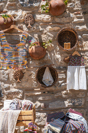 A rustic market stall display with a variety of handmade woven clothes, terracotta pots, and baskets hanging on a weathered stone wall in Turkey.の写真素材