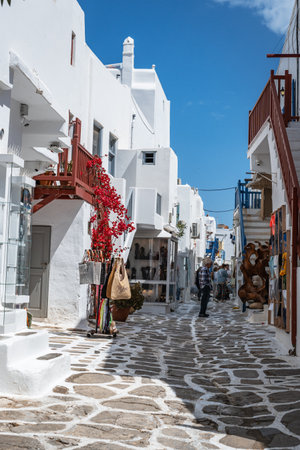 A narrow alley with a traditional stone path winds between sunlit, whitewashed buildings and a vibrant blue door in a Greek island village.の写真素材