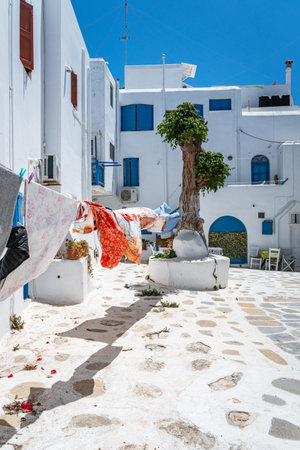 A sunlit alley with a blue door and a staircase in a traditional Greek village. High quality photo. A narrow, sun-drenched cobblestone alley with traditional whitewashed buildings, a blue door, and an external staircase in a charming Greek village.の写真素材