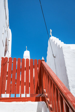A vertical view of a charming Greek island alleyway with whitewashed buildings, traditional colorful stairs, and a clothesline under a clear blue sky.の写真素材