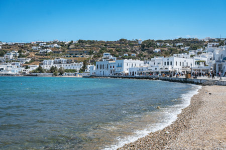 A view of the Mykonos harbor with traditional boats and whitewashed village. High quality photo. A classic view of the Mykonos harbor, featuring various boats in the calm blue water and the iconic whitewashed village climbing the hillside under a clear sky.の写真素材
