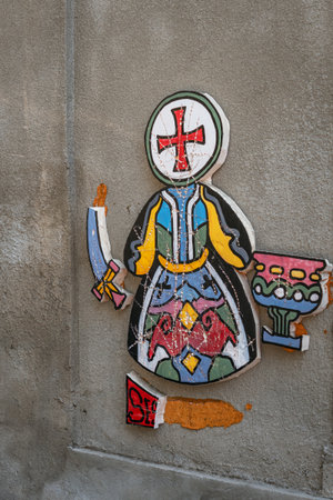 A damaged piece of colorful urban art depicting a stylized figure with a cross, a chalice, and a broken sword.の写真素材